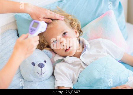 Enfant malade au lit. La mère s'est mise à vérifier sur un enfant malin. Un petit garçon qui a de la fièvre se sent malade. Maman avec thermomètre et médicaments contre la toux. Banque D'Images