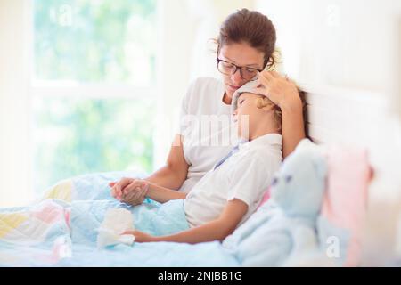 Enfant malade au lit. La mère s'est mise à vérifier sur un enfant malin. Un petit garçon qui a de la fièvre se sent malade. Maman avec thermomètre et médicaments contre la toux. Banque D'Images