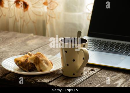 crêpes caillé sur une assiette, une tasse de thé et un ordinateur portable sur une table en bois Banque D'Images