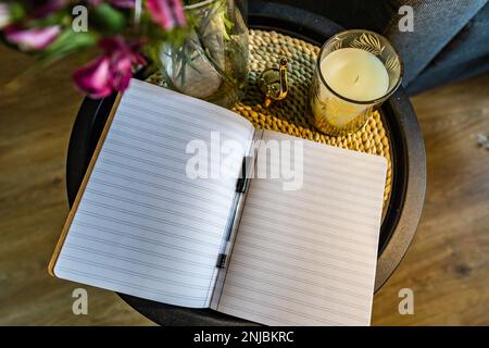 Petit bloc-notes A5 avec lignes se trouve sur une petite table basse avec un crayon noir à côté d'un vase avec des fleurs et une petite bougie Banque D'Images