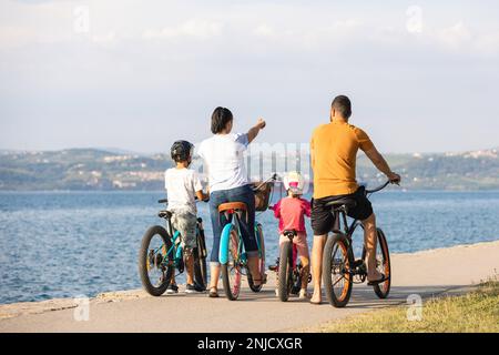 Deux enfants avec leurs parents, cyclistes amateurs, faire une pause et regarder le paysage marin pendant une journée d'été claire Banque D'Images