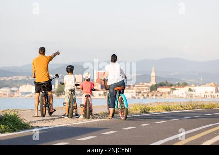 Deux enfants avec leurs parents, cyclistes amateurs, faire une pause et regarder le paysage marin pendant une journée d'été claire Banque D'Images