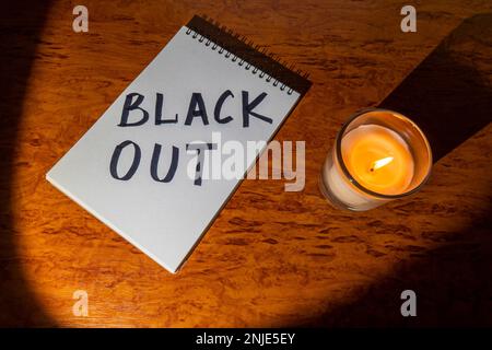 Bloc-notes avec l'inscription « Blackout » et une bougie allumée dans un pot en verre sur une table en bois, éclairée par un spot. Concept de coupure de courant Banque D'Images