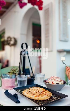 Pita grec doux, farci de fromage parsemé de graines de sésame, miel, servi avec de la salade grecque et de l'eau dans un café extérieur Banque D'Images