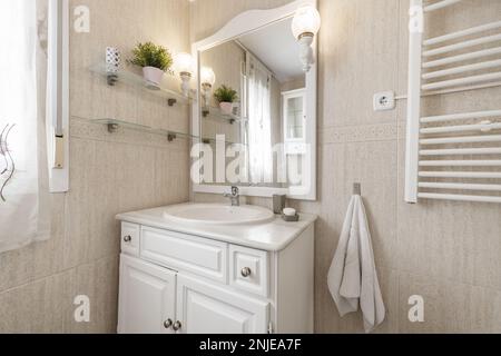 Salle de bains avec murs et sols carrelés de crème, meuble de salle de bains en bois blanc, lavabo en porcelaine blanche avec miroir et cadre en bois assorti Banque D'Images