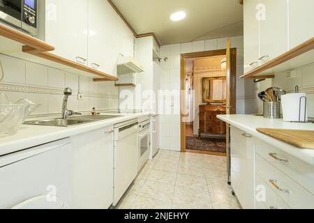 Cuisine avec meubles blancs avec poignées en métal et bois pour assortir les corniches et les moulures, electromesivos de divers blancs intégrés et carreaux de lumière Banque D'Images