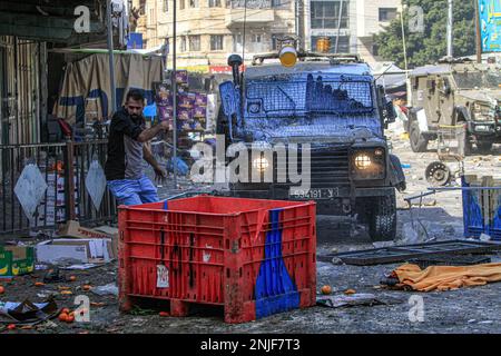 Naplouse, Palestine. 22nd févr. 2023. Des jeunes Palestiniens jettent des marchandises et des légumes sur les véhicules de l'armée israélienne lors des affrontements au marché des légumes dans la vieille ville de Naplouse, en Cisjordanie occupée. Des affrontements ont éclaté entre les Palestiniens et l'armée israélienne après que l'armée israélienne ait éclaté dans le refuge dans lequel des hommes armés palestiniens des groupes Lions de Den se cachaient dans la vieille ville de Naplouse, tuant quatre hommes armés et six civils qui étaient présents sur le marché pendant le raid. Crédit : SOPA Images Limited/Alamy Live News Banque D'Images