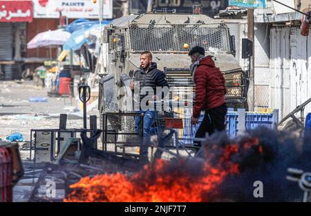 Naplouse, Palestine. 22nd févr. 2023. Des jeunes Palestiniens brûlent des pneus devant le véhicule de l'armée israélienne lors des affrontements sur le marché des légumes dans la vieille ville de Naplouse, en Cisjordanie occupée. Des affrontements ont éclaté entre les Palestiniens et l'armée israélienne après que l'armée israélienne ait éclaté dans le refuge dans lequel des hommes armés palestiniens des groupes Lions de Den se cachaient dans la vieille ville de Naplouse, tuant quatre hommes armés et six civils qui étaient présents sur le marché pendant le raid. Crédit : SOPA Images Limited/Alamy Live News Banque D'Images