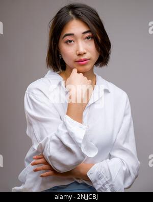 Portrait à moitié corps de la jeune femme asiatique magnifique debout devant un arrière-plan blanc | bras enveloppés autour de la poitrine Banque D'Images