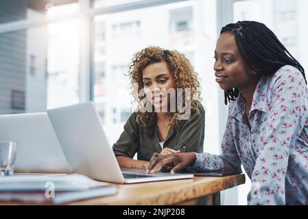 Les idées circulent entre les deux. deux jeunes collègues utilisent un ordinateur portable dans un bureau moderne. Banque D'Images