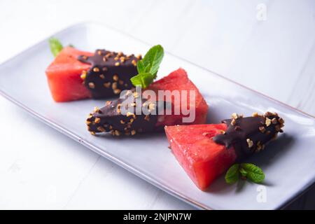 Morceaux de pastèque fraîche trempée dans du chocolat et recouverte d'amandes caramélisées. Banque D'Images