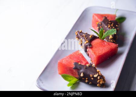 Morceaux de pastèque fraîche trempée dans du chocolat et recouverte d'amandes caramélisées. Banque D'Images