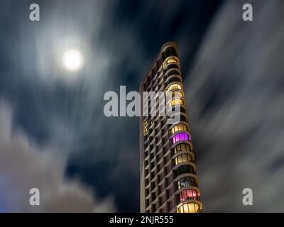 Une vue imprenable sur un bâtiment lumineux et lumineux lors d'une nuit nuageux sur fond de pleine lune Banque D'Images