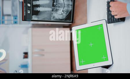 Vidéo verticale : gros plan de l'écran vert horizontal sur une tablette numérique au cabinet du dentiste. Stomatologue utilisant un modèle de maquette et un fond isolé sur le gadget pour la dentisterie et les soins buccaux Banque D'Images