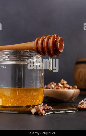 Composition de la cuisine : pot en verre et tonneau en bois avec miel biologique sain, balancier en bois et bol de noix sur fond sombre Banque D'Images