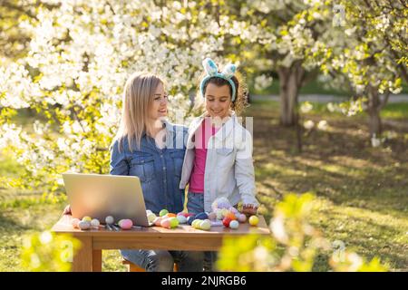 mère et fille peignent des œufs de pâques avec un ordinateur portable, enregistrer des leçons sur une webcam avec un ordinateur portable. la mère et la fille se préparent pour les vacances Banque D'Images