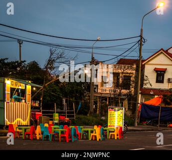 Street food stand dans un parking avec de petites chaises et tables vietnamiennes colorées en plastique servant de la nourriture vietnamienne. Banque D'Images