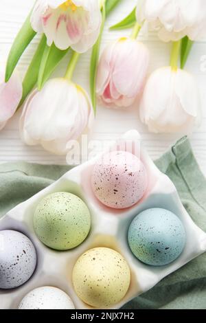 Porte-oeufs de Pâques peint couleurs pastel et tulipes roses sur fond blanc en bois. Vue de dessus. Espace pour le texte. Banque D'Images