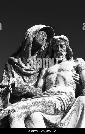 Une statue en pierre naturelle réplique de la célèbre Pieta de la Vierge Marie de Michel-Ange tenant le corps de son fils Jésus dans un monochrome noir et blanc. Banque D'Images