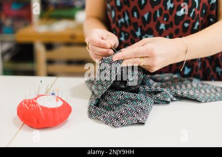 Anonyme femme designer en chemise décontracté modèle de couture sur le tissu avec aiguille dans l'atelier créatif Banque D'Images