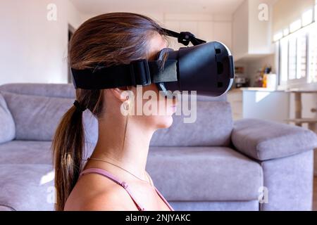 Vue latérale de la femme courte ciblée dans des lunettes de sport et VR assis méditant dans le salon Banque D'Images