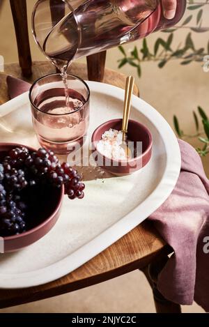 Grand angle de récolte anonyme personne versant de l'eau fraîche dans le verre placé sur plateau blanc avec des raisins noirs et dessert le jour chaud d'été Banque D'Images