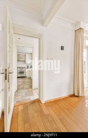 Intérieur de maison spacieuse avec porte blanche ouverte à la cuisine du hall avec parquet en lumière du jour Banque D'Images