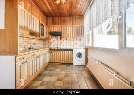 Décoration intérieure de cuisine rustique avec mobilier en bois et appareils modernes avec cuisinière et hotte avec lave-linge intégré près du hall avec portes Banque D'Images