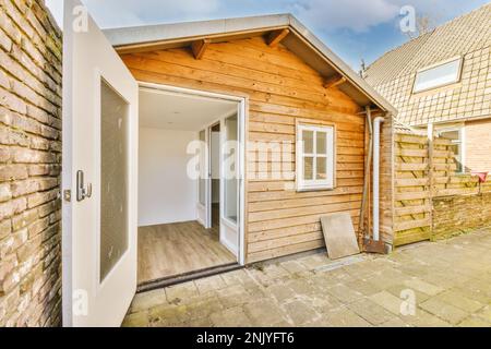 Extérieur de cour de petite maison rustique avec porte blanche ouverte et fenêtre avec façade en bois et carrelage en béton près du mur de briques Banque D'Images