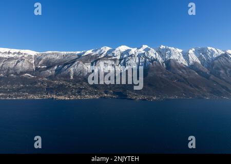 Vue à couper le souffle sur les eaux claires du lac de Garde, sur fond de montagnes alpines majestueuses, baignées de neige pendant une journée d'hiver ensoleillée Banque D'Images