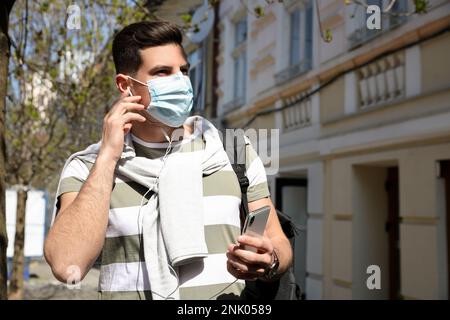 Homme dans un masque de protection écoutant un livre audio dans la rue de la ville Banque D'Images