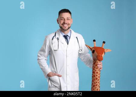 Pédiatre avec girafe jouet et stéthoscope sur fond bleu clair Banque D'Images