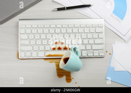 Tasse de café renversé sur le clavier de l'ordinateur sur le bureau blanc, plat Banque D'Images