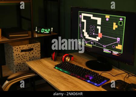 Ordinateur moderne et clavier RVB sur une table en bois dans une pièce sombre Banque D'Images