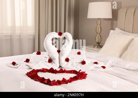 Belle composition sur le lit. Cygnes faits de serviettes et pétales de rose disposés en forme de coeur Banque D'Images