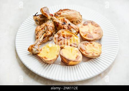 Poulet cuit en morceaux avec des pommes de terre et des oignons sur un plat blanc. Cuisine maison. Aliments sains, cuits sans huile ni sel. Banque D'Images