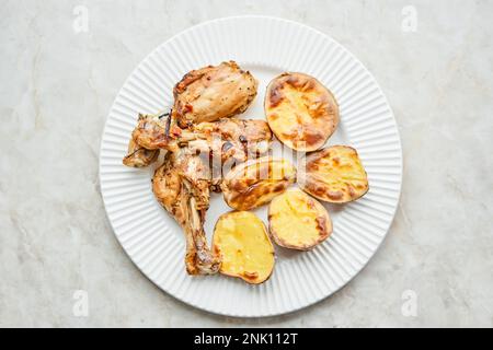 Poulet cuit en morceaux avec des pommes de terre et des oignons sur un plat blanc. Cuisine maison. Aliments sains, cuits sans huile ni sel. Banque D'Images