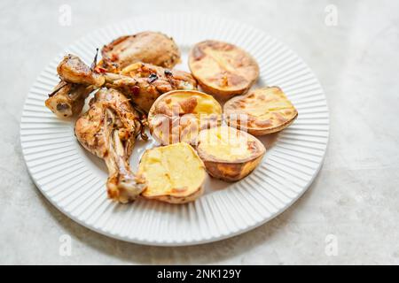 Poulet cuit en morceaux avec des pommes de terre et des oignons sur un plat blanc. Cuisine maison. Aliments sains, cuits sans huile ni sel. Banque D'Images