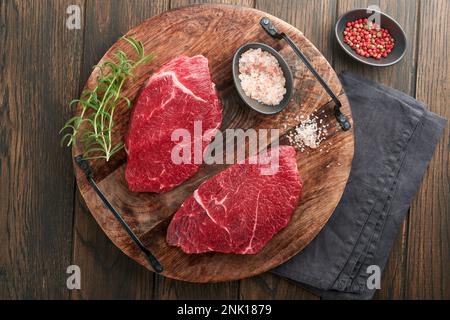 Steak de bœuf cru. Steak de Ribeye frais et cru marbré avec romarin, sel et poivre sur planche à découper sur fond de béton foncé. Steak de bœuf cru et épices Banque D'Images