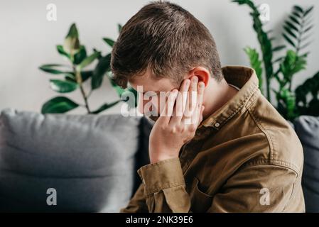 Malsain triste homme caucasien 30s souffrant d'otite douloureuse. Concept des soins de santé, de la médecine et des acouphènes. Gros plan sur le jeune homme barbu havi Banque D'Images