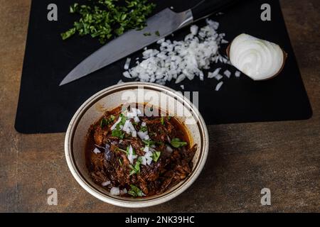 Un bol de viande de bœuf bigria cuite lentement et braisée dans un bol d'époque avec des oignons hachés, de la coriandre, des poivrons guajillo et du bouillon Banque D'Images