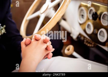 les décorations et les détails sur la voiture pour le mariage entremêlent les mains de la mariée et du marié à l'intérieur d'une voiture vintage blanche avec un volant en bois Banque D'Images