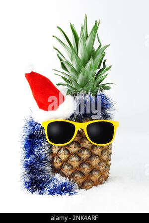 Ananas fruit tropical en costume chapeau de Père Noël et lunettes de soleil jaunes sur la neige. Isolé sur un fond blanc. Carte postale concept pour le nouvel an an Banque D'Images