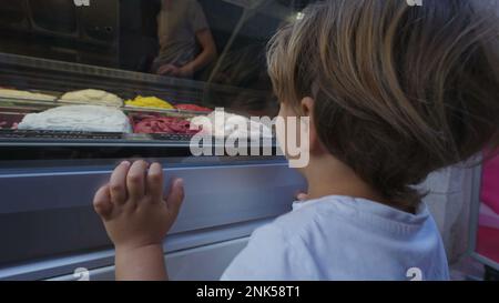 Enfant assis sur le comptoir de glace et regardant les saveurs de glace. Compteur réexonéré Banque D'Images