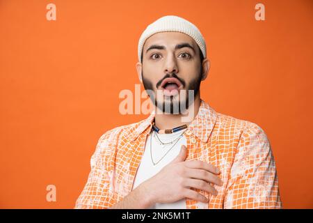 homme barbu étonné en bonnet blanc regardant la caméra isolée sur orange, image de stock Banque D'Images