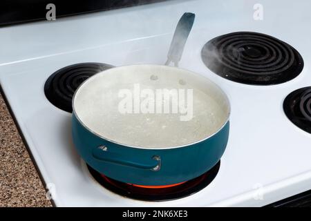 Plan horizontal d'un pot bleu sur un dessus de poêle tenant l'eau bouillante avec la vapeur qui monte. Banque D'Images