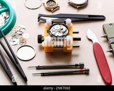 ouvrir la montre mécanique dans le support jaune et les outils sur la table en bois dans l'atelier horloger Banque D'Images