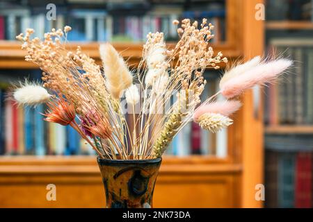 vue latérale du bouquet de plantes séchées dans un vase gros plan avec une bibliothèque floue sur le fond Banque D'Images