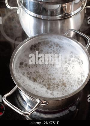 cuisson des pâtes dans l'eau bouillante dans une casserole sur une cuisinière en céramique dans la cuisine maison Banque D'Images
