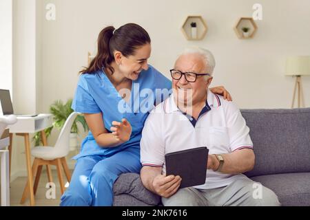 Jeune femme aide-soignant et homme âgé utilisant une tablette numérique ensemble dans une maison de soins. Banque D'Images